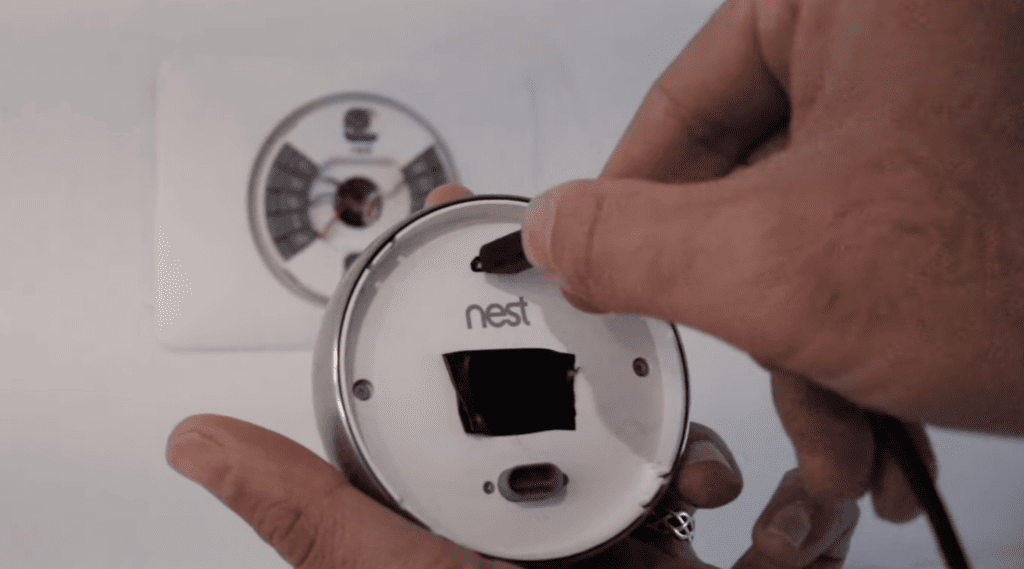 Photo of a person plugging a USB charger into a Nest thermostat removed from the wall