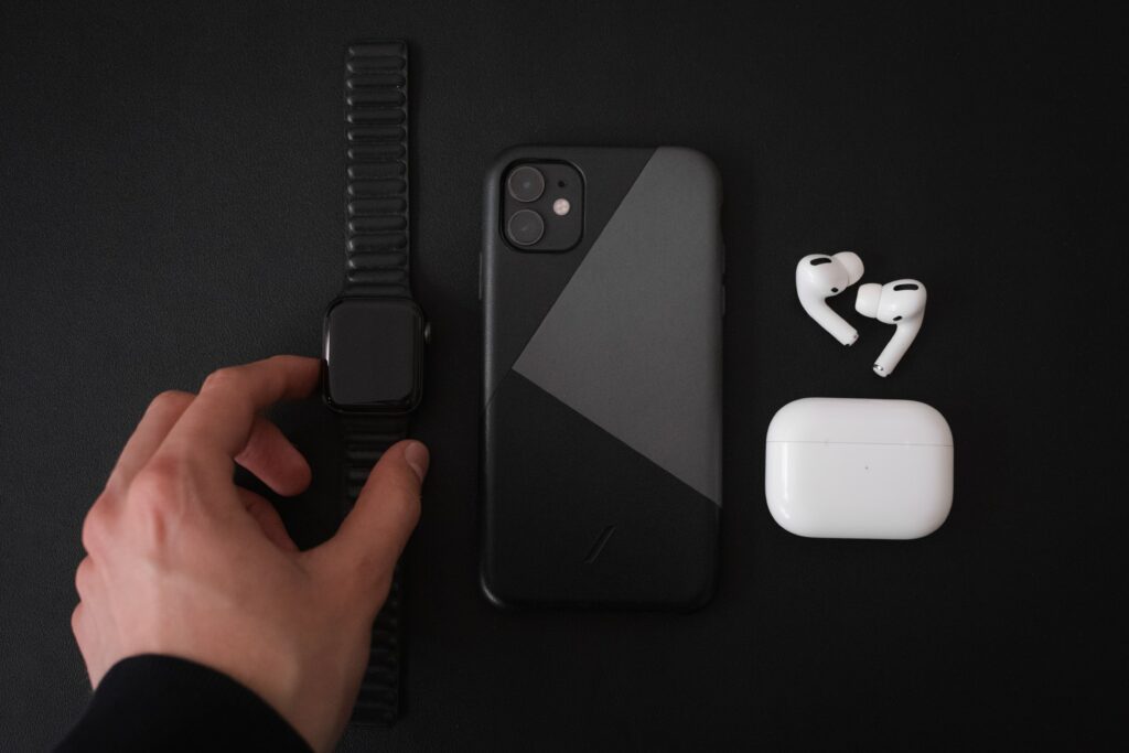 Apple products laying on black background with someone holding the Apple watch