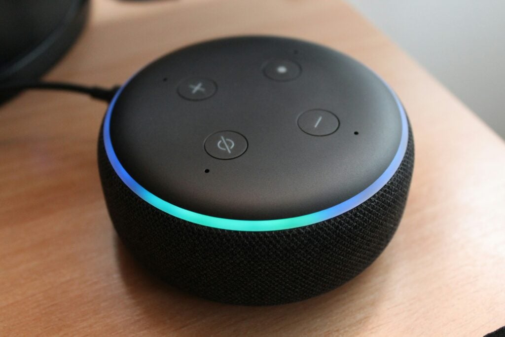 A black Alexa echo dot 3rd gen on a wooden table