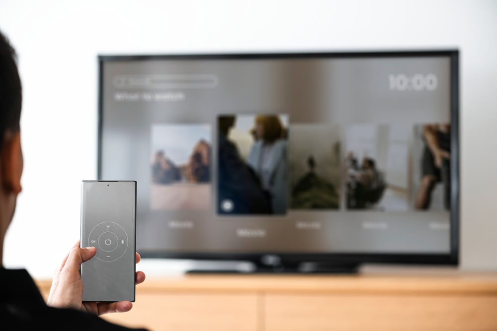 man changing TV channels using a smartphone as a remote